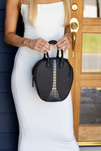 Load image into Gallery viewer, Lady in long white bodycon dress holds a black oval vegan leather shoulder bag with croc print inset.
