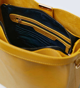 The inside of a mustard yellow vegan leather shoulder bag showing blue recycled plastic lining with a gold internal zip and gold hardware.