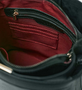 The inside of a black vegan leather shoulder bag showing a red recycled plastic lining and gold zip and hardware.