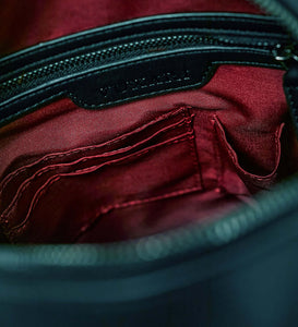 The inside of a black vegan leather shoulder bag showing a red recycled plastic lining and gunmetal zip and hardware.