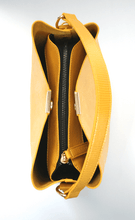 Load image into Gallery viewer, A top down view of a mustard yellow shoulder bag showing the recycled vegan leather outer, dark, blue recycled plastic lining and gold hardware.
